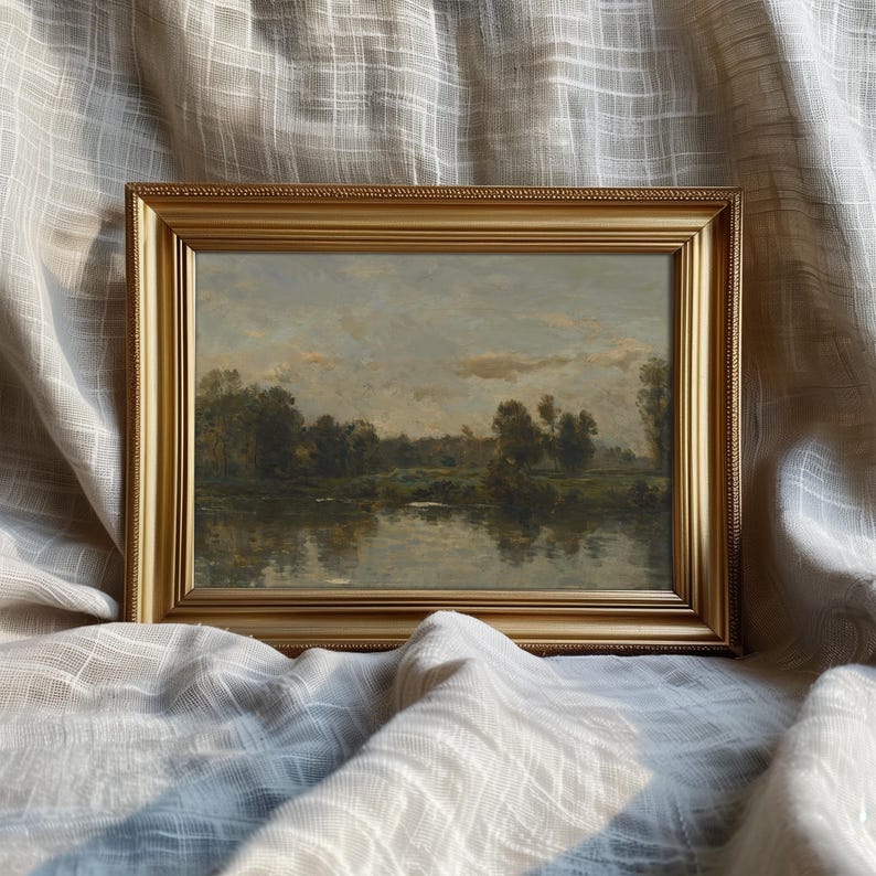 May include: A framed landscape painting depicting a river scene with trees and a cloudy sky. The frame is gold with a decorative border.
