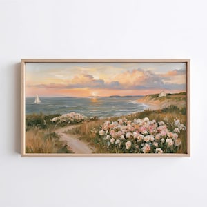 May include: A rectangular framed landscape painting depicting a coastal scene at sunset. The artwork features a sailboat on the water, a small house on a cliff, and a foreground filled with blooming pink and white flowers along a dirt path.