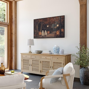 May include: A living room with a light wood cabinet, a white armchair, and a framed painting of children trick-or-treating in a forest. The painting features a dark background with glowing pumpkins and lanterns.