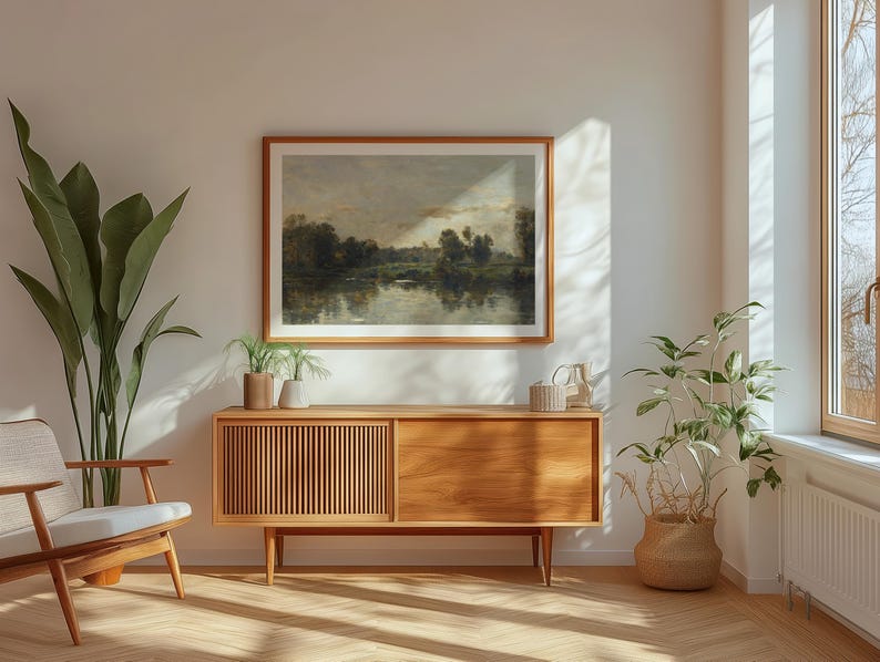May include: A wooden cabinet with two doors and a drawer, featuring a light wood finish and a mid-century modern style. The cabinet is placed in a living room setting with a large painting of a landscape scene hanging above it.