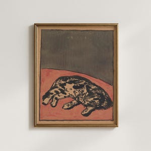 Puede incluir: Obra de arte enmarcada que representa un gato negro y marrón tumbado sobre una superficie roja, con un fondo gris oscuro. La obra está en un marco dorado, ideal para la decoración del hogar.