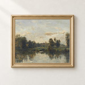 May include: A landscape painting in a gold frame depicting a calm river reflecting a line of dark green trees under a cloudy, pale blue and beige sky. The artwork features soft brushstrokes and muted earth tones throughout the scene.