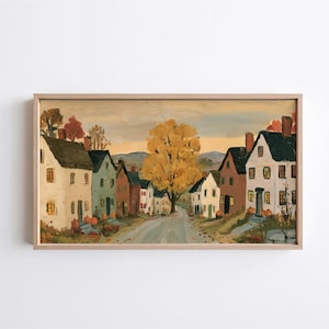 May include: A framed landscape painting depicting a small town street during autumn. The scene features multi-colored houses, a large central tree with golden yellow foliage, and orange pumpkins scattered along the roadside under a pale sky.
