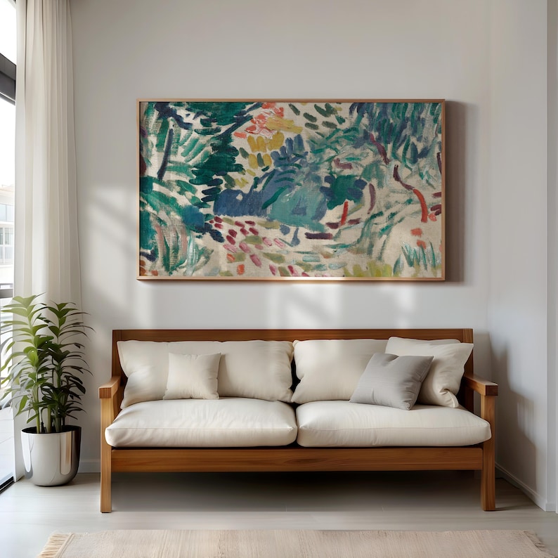 May include: A framed abstract painting with a wooden frame hangs above a wooden sofa with white cushions. The painting features a colorful landscape with green, blue, yellow, and red brushstrokes. A potted plant sits to the left of the sofa.