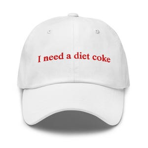 Puede incluir: Gorra de béisbol blanca con la frase bordada en rojo "I need a diet coke". La gorra tiene una visera curva y un botón en la parte superior. Un accesorio casual.