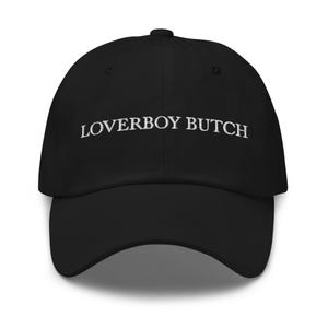 Puede incluir: Gorra de béisbol negra con el texto bordado "LOVERBOY BUTCH" en blanco. La gorra tiene una visera curva y un ajuste estructurado. Un accesorio clásico e informal.