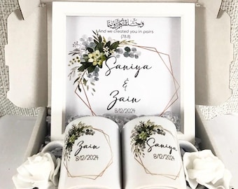 May include: A white gift box with a framed print featuring a floral design and the names "Saniya & Zain" with the date "8/12/2024". The box also contains two white mugs with the same floral design and names, and a white rose.