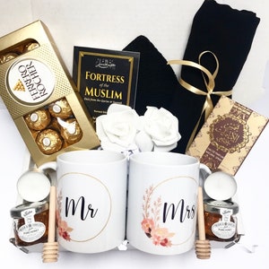 Könnte beinhalten: Ein Geschenkkorb in Schwarz-Gold. Er enthält zwei weiße Tassen mit den Worten "Mr" und "Mrs" darauf, ein Buch mit dem Titel "Fortress of the Muslim", eine Schachtel Pralinen, einen schwarzen Schal, zwei weiße Rosen und zwei kleine Honiggläser.