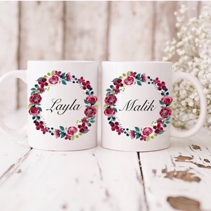 May include: Two white ceramic mugs with floral wreaths and the names "Layla" and "Malik" in black script.