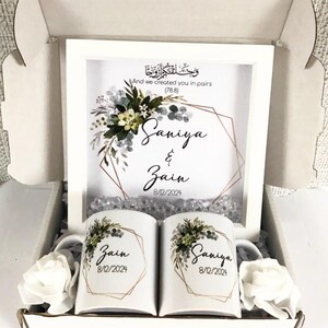 May include: A white gift box with a white frame containing a floral design and the names "Saniya & Zain" with the date "8/12/2024". The box also contains two white mugs with the same floral design and names, one with "Zain" and the other with "Saniya".