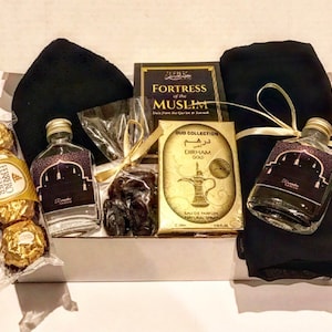 Könnte beinhalten: Eine Geschenkbox gefüllt mit Artikeln für eine religiöse Feier. Die Box enthält ein Buch mit dem Titel "Fortress of the Muslim", eine Parfümflasche, eine kleine Flasche mit Flüssigkeit, ein schwarzes Kopftuch und eine Schachtel Pralinen.