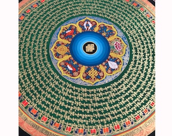 May include: A circular mandala with a green background and gold lettering. The centre of the mandala features a blue and gold lotus flower with a red centre. The lotus flower is surrounded by a circle of gold lettering.