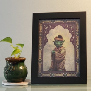 May include: A framed print of a green, cartoon character wearing a hat and robe. The character is standing in a doorway with a decorative archway. The print has a dark brown frame and a white mat.