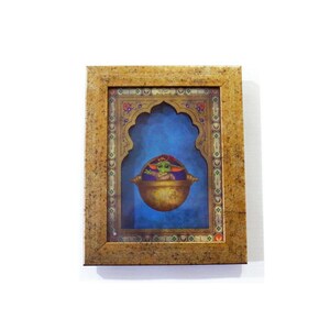 May include: A framed illustration of a green alien character in a floating pod, set against a blue background with a gold ornate frame.