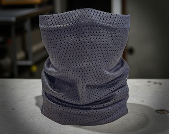 May include: A gray, perforated neck gaiter, designed to be worn around the neck and lower face. The fabric has a mesh-like appearance with small holes throughout. The gaiter is made of a flexible material and is likely used for sun protection or as a face covering.
