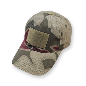 May include: A baseball cap featuring a camouflage pattern in shades of olive green, tan, and dark maroon. The cap includes a rectangular hook-and-loop patch panel on the front crown and a small square patch panel on the top, with ventilation eyelets.
