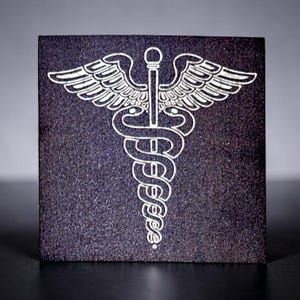 May include: A square, dark gray tile with a white Caduceus symbol. The symbol features two snakes entwined around a staff with wings at the top. The tile has a textured surface.