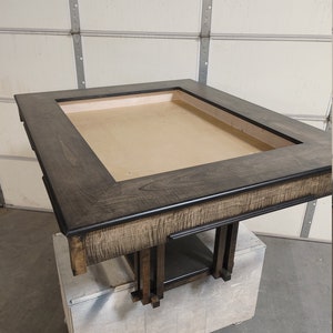 Könnte beinhalten: Ein dunkelbrauner Holztisch mit einer rechteckigen Tischplatte und einem erhöhten Rand. Der Tisch hat ein schlichtes, modernes Design mit einer schwarzen Beize. Der Tisch steht auf einer Holzkiste.