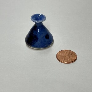 May include: A small, blue and white ceramic vase with a wide mouth and a rounded base. The vase is about the size of a US penny.