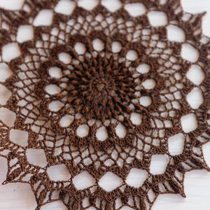 May include: A brown crocheted doily with a circular design and a delicate, lacy pattern.