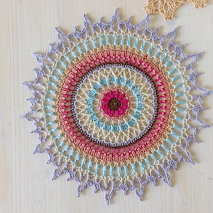 May include: A colorful crocheted mandala with a multi-colored center and a light purple outer edge.