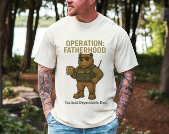 May include: A white t-shirt with a cartoon illustration of a bear wearing sunglasses and holding a coffee mug that says "#1 Dad". The text on the shirt reads "Operation: Fatherhood Tactical. Dependable. Dad."