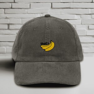 Puede incluir: Una gorra de b&eacute;isbol de pana gris oscuro con un dise&ntilde;o bordado de pl&aacute;tanos amarillos y el texto "that's".