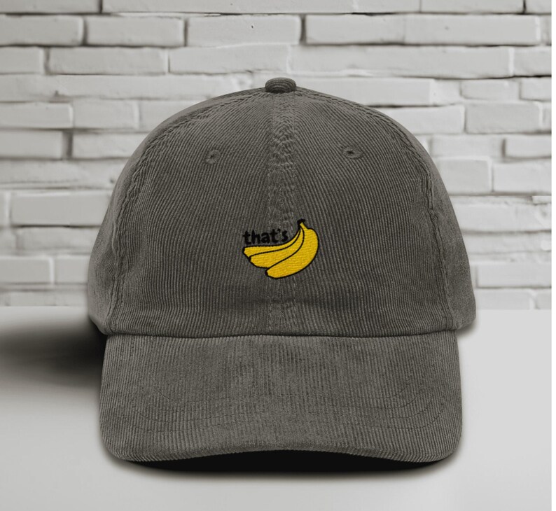 Puede incluir: Una gorra de b&eacute;isbol de pana gris oscuro con un dise&ntilde;o bordado de pl&aacute;tanos amarillos y el texto "that's".