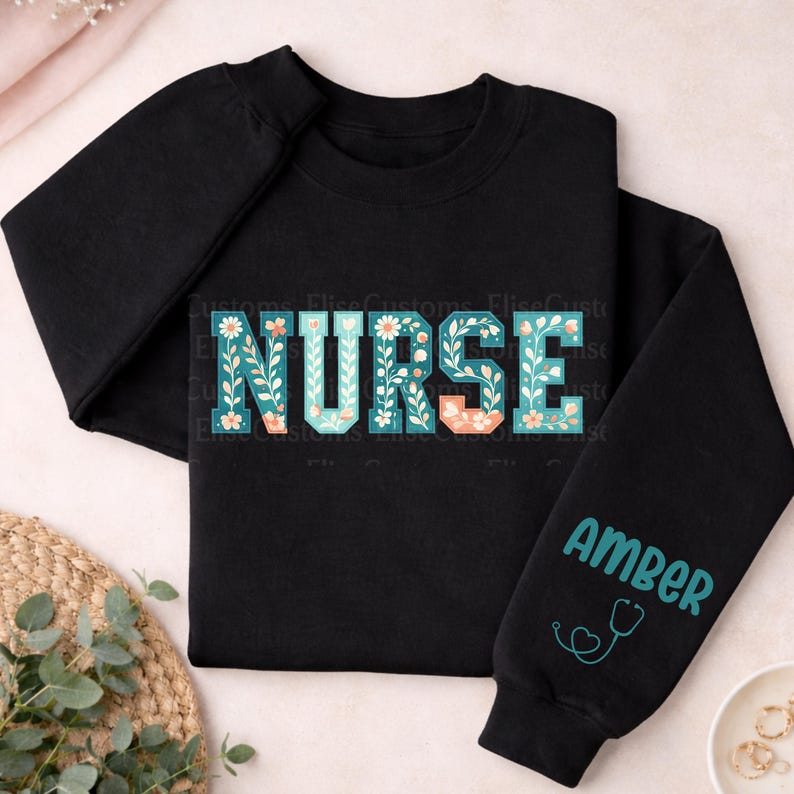 May include: Black sweatshirt with the word "NURSE" in teal letters decorated with floral designs. The sleeve has the name "Amber" in teal, along with a teal stethoscope graphic. The sweatshirt is made of a soft material.