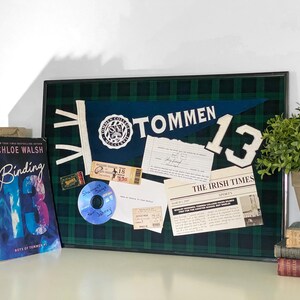 Puede incluir: Un tablero de anuncios enmarcado de cuadros verdes y negros con un banderín azul y blanco que dice "TOMMEN 13". También hay entradas, un recorte de periódico y un CD en el tablero.