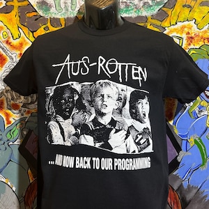 May include: Black t-shirt with a white graphic print of a band called "Aus-Rotten". The graphic features a black and white photo of four people with the text "...and now back to our programming".