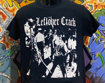 May include: Black t-shirt with a white graphic print of a band called "Leftover Crack". The graphic features a group of people in a black and white silhouette.