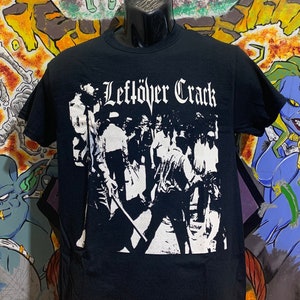 May include: Black t-shirt with a white graphic print of a band called "Leftover Crack". The graphic features a group of people in a black and white silhouette.