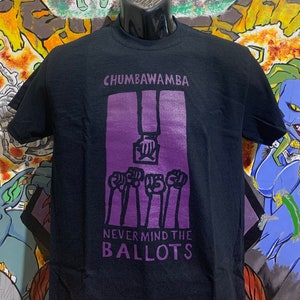 May include: Black t-shirt with a purple graphic print of raised fists and the text "Chumbawamba Never Mind The Ballots".