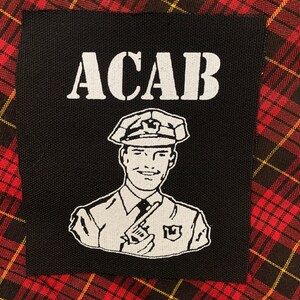 May include: Black patch with white text that reads "ACAB" and a cartoon image of a police officer with a gun and a walkie-talkie.