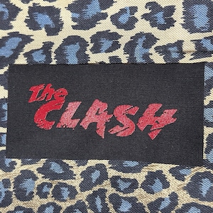 May include: A black patch with the words "The Clash" in red lettering on a leopard print background.