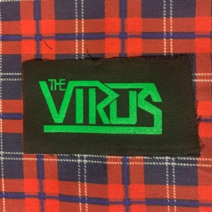 May include: Black rectangular patch with the words "THE VIRUS" in green block letters. The patch is set against a red, blue, and white plaid background.