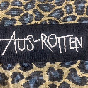 May include: A black patch with white text that reads "AUS-ROTTEN".