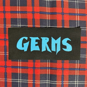 May include: Black patch with the word "GERMS" in blue lettering.