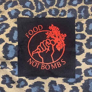 May include: A black patch with red text and a red graphic. The text reads "FOOD NOT BOMBS" and the graphic is a fist holding a carrot.