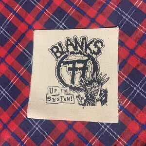 May include: A white fabric patch with black text and an illustration. The text reads "Blanks 77 Up The System!" The illustration is of a cartoon character with spiky hair and a mischievous grin.
