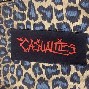 May include: A black patch with white stitching and the text "THE CASUALTIES" in red lettering.