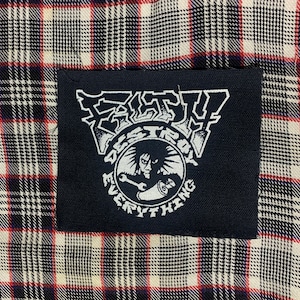 May include: Black and white patch with the text "Fast" and "Destroy Everything" in a circle around a skull with a wrench. The patch is sewn onto a plaid fabric.