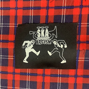 May include: Black and white patch with a trombone, two figures in suits, and the text "TTT Ska Against Racism".