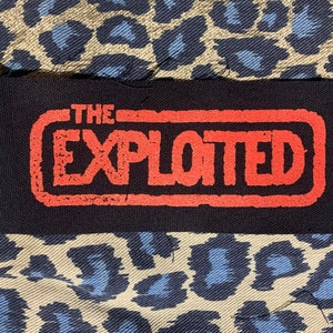 May include: A black fabric patch with a red rectangular border and the text "THE EXPLOITED" in red.