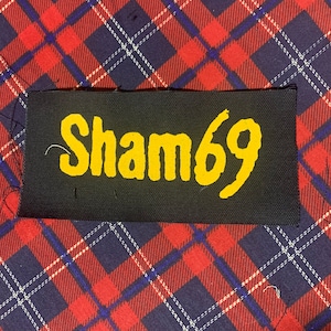 May include: A black fabric patch with the text "Sham69" in yellow lettering.