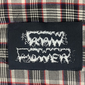 May include: A black patch with white text that reads "RAW POWER" in a stylized font.