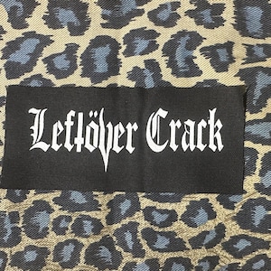 May include: Black patch with white text that reads "Leftover Crack" on a leopard print fabric background.