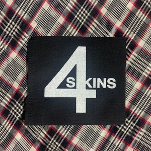 May include: A black patch with white text that reads "4SKINS" on a plaid fabric background.