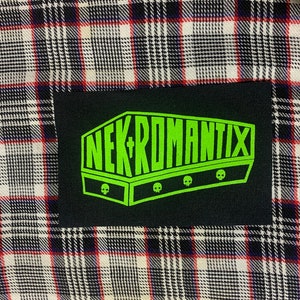 May include: A black and green patch with the text "NEKROMANTIX" in a coffin-shaped design. There are three skull graphics below the text.